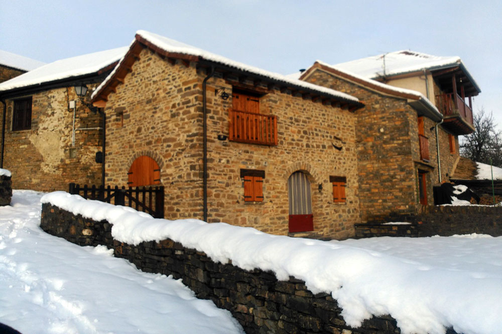 Casa rústica con fachada de piedra con el tejado y la entrada cubiertos de nieve
